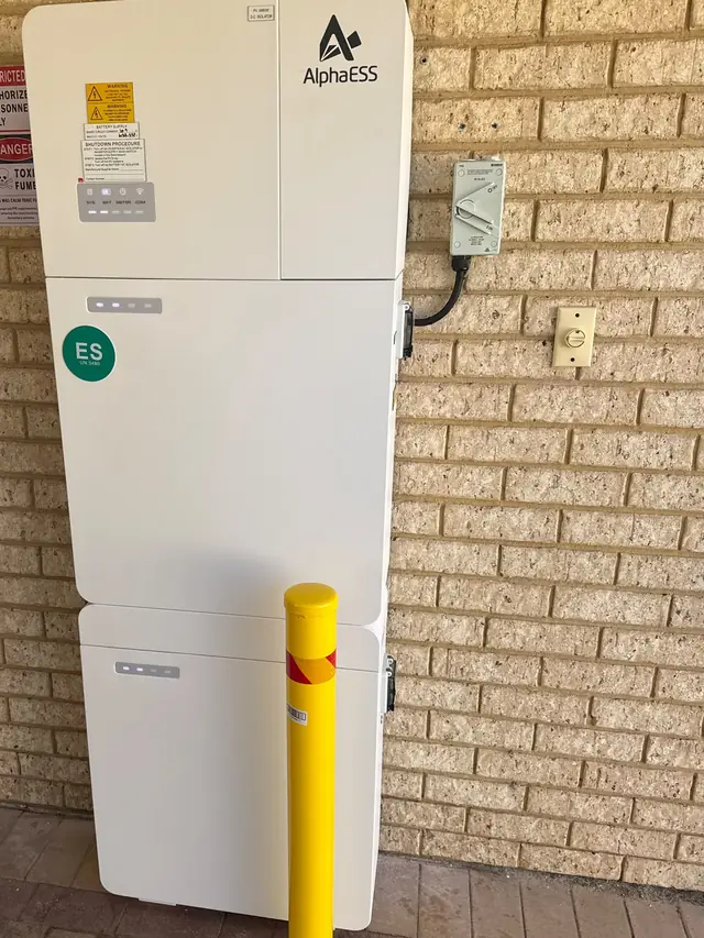 AlphaESS battery system installed against a brick wall with a safety bollard