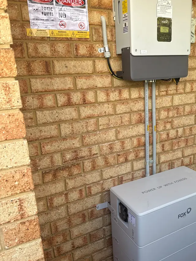 Fox ESS battery and inverter installed on a yellow brick wall